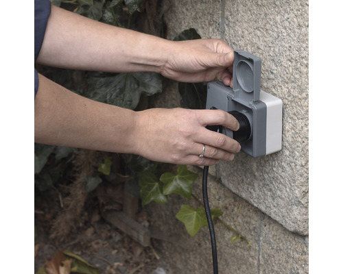 Une personne branche une prise dans une prise extérieure