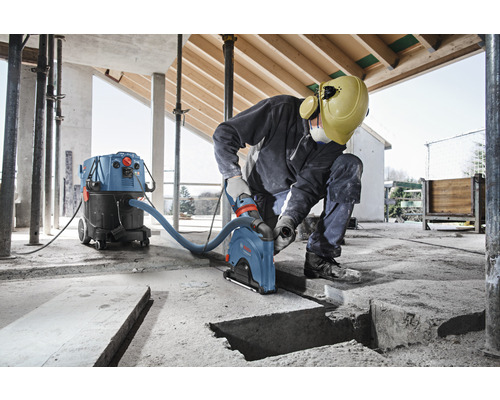 Ein Arbeiter, der eine Mauernutfräse in einem Gebäude mit einem Industriestaubsauger verwendet.