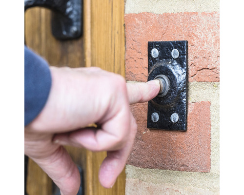 Eine Person drückt auf eine Türklingel an einer Backsteinmauer.