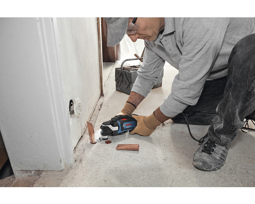 Un homme coupe un tuyau de cuivre dans une pièce avec un outil multifonction.