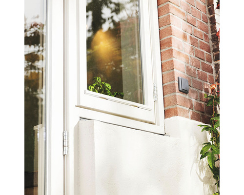 Nahaufnahme eines weißen Fensters mit Beschlägen und einer Außensteckdose an einer Ziegelwand