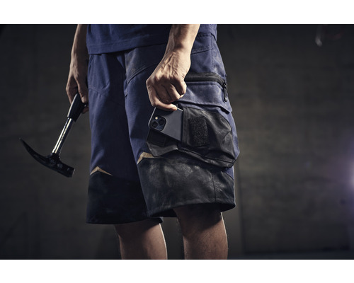 Homme portant un short de travail, un téléphone portable dans la poche et un marteau à la main