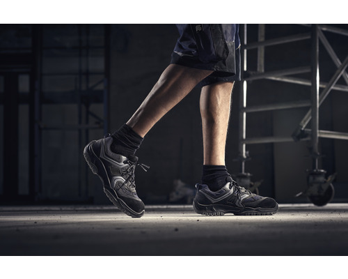 Personne en chaussures de travail et short devant un échafaudage.