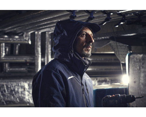 Un artisan avec une veste et une visseuse sans fil travaille dans un bâtiment.