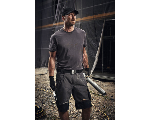 Un artisan porte des vêtements de travail avec un short, un t-shirt, une ceinture et des gants sur un chantier