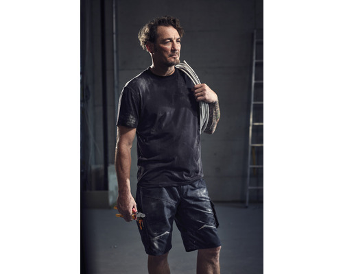 Un homme portant des câbles électriques sur l''épaule et tenant une pince à la main porte un pantalon de travail.