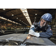 Mann schleift Metall mit einem Winkelschleifer und trägt dabei Schutzkleidung in einer Werkshalle.