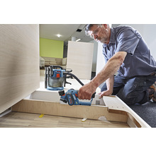 Artisan travaillant avec un rabot sur une pièce de bois, un aspirateur est prêt