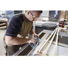Un homme portant des lunettes de sécurité coupe un plan de travail avec un outil multifonction.