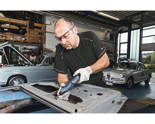 Homme travaillant une portière de voiture avec un outil multifonction dans un atelier