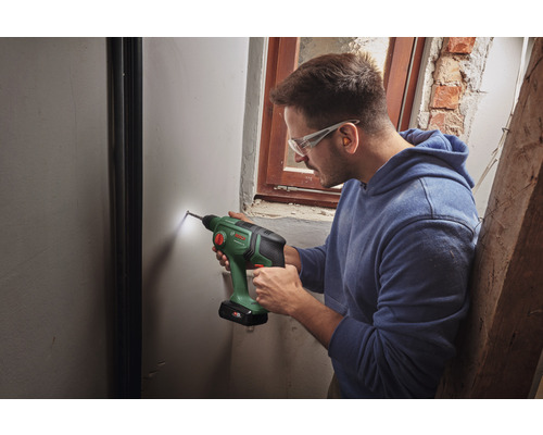 Un homme perce un trou dans un mur avec une perceuse sans fil.