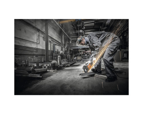 Un homme en équipement de protection coupe du métal avec une meuleuse d''angle dans un atelier, produisant des étincelles.