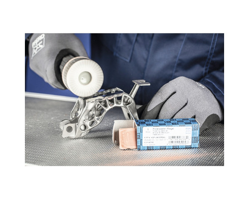 Un homme polit une pièce métallique avec une meule à polir, ainsi qu''un pain de pâte à polir.