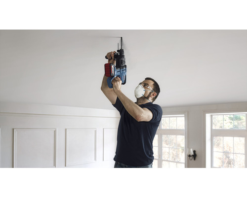 Un homme perce un trou dans le plafond avec une perceuse à percussion.