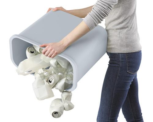 Une personne vide une poubelle remplie de canettes, de plastique et de verre.