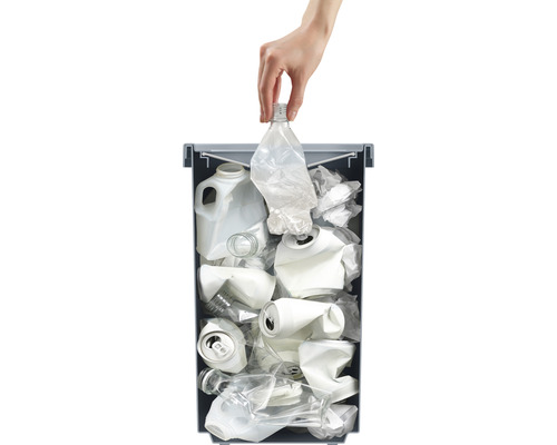 Une main jette une bouteille en plastique dans une poubelle de recyclage contenant d''autres matériaux recyclables.