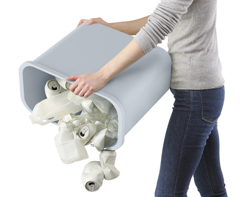 Femme vide une poubelle contenant des boîtes de conserve et des bouteilles en plastique