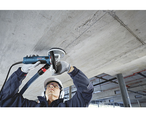 Ein Mann schleift eine Betondecke mit einem Deckenschleifer mit Absaugvorrichtung.
