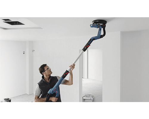 Un homme ponce un plafond avec une ponceuse à long manche dans une pièce.