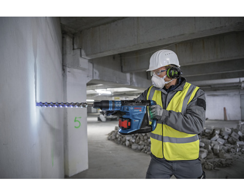 Handwerker bohrt mit einem Bohrhammer in eine Wand. Der Bohrhammer ist blau.