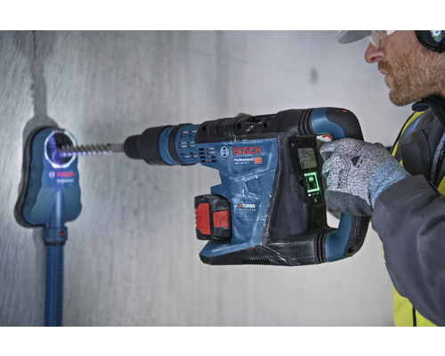 Mann bohrt mit einem Boschhammer ein Loch in eine Wand mit Staubabsaugung