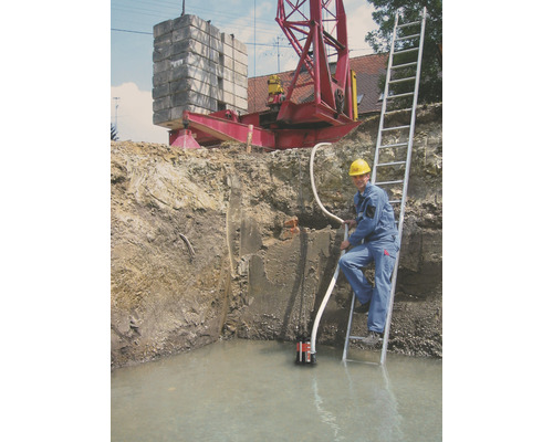 Fouille avec de l''eau, pompe submersible, ouvrier sur échelle et grue en arrière-plan