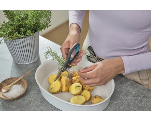 Une personne coupe du romarin avec des ciseaux au-dessus d''un saladier de pommes de terre.