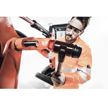 Un homme portant des lunettes de protection utilise un marteau pour réparer une machine.