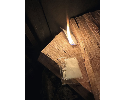 Auf einem Holzstück brennt eine Flamme neben einer Verpackungseinheit mit Wachs