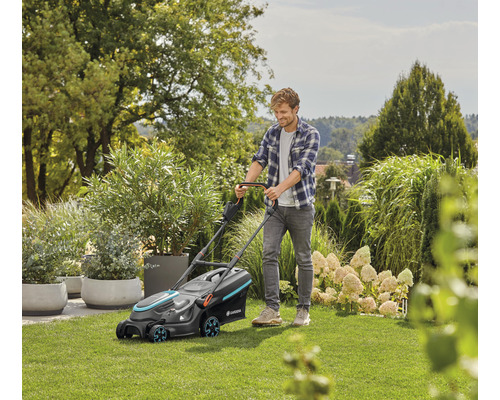 Ein Mann mäht Rasen mit einem Gardena Rasenmäher im Garten.