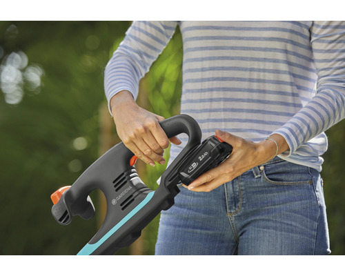 Eine Frau befestigt einen 2,0-Ah-Akku an einem Gardena Trimmer.