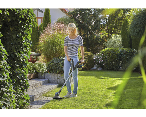 Frau benutzt Rasentrimmer im Garten zur Rasenpflege.