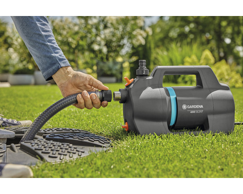 Eine Person schliesst einen Wasserschlauch an eine Gardena Gartenpumpe 4200 Silent im Garten an.