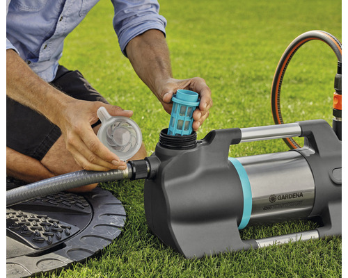 Eine Person setzt einen Filter in eine Gardena Gartenpumpe auf einer Rasenfläche ein.