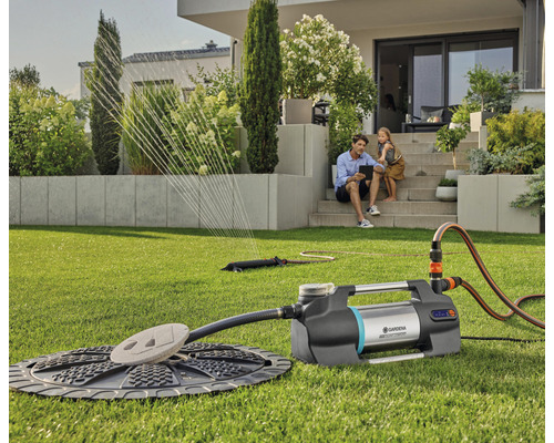 Gartenbewässerung mit Regner und Pumpe auf Rasenfläche vor Haus