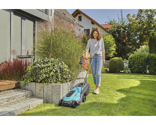 Frau mäht Rasen mit einem Rasenmäher im Garten.