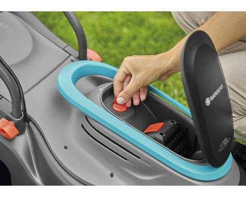 Detailansicht eines Rasenmähers mit geöffnetem Akkufach und einer Hand, die einen roten Knopf drückt