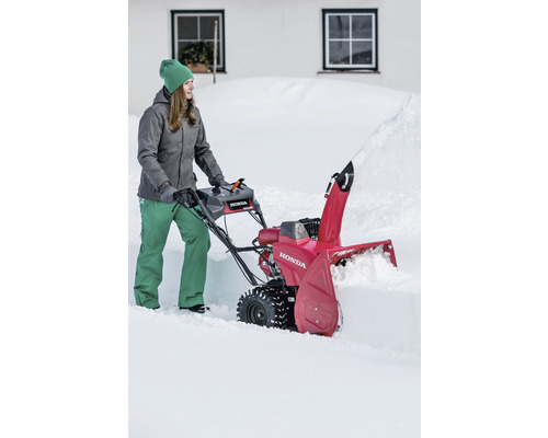 Frau bedient eine rote Schneefräse der Marke Honda im Schnee.