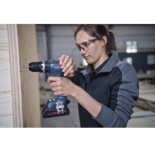 Une femme visse une vis dans une planche de bois avec une visseuse sans fil. Logo Bosch.