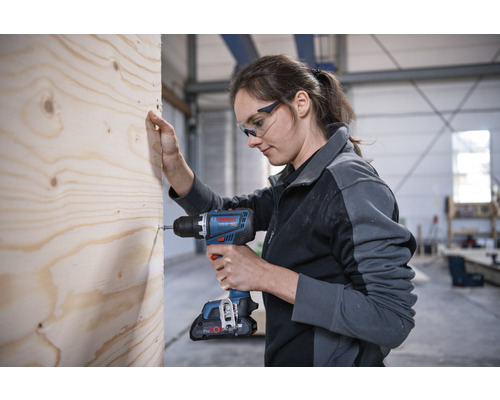 Frau schraubt Schraube mit Akku-Bohrschrauber in Holz