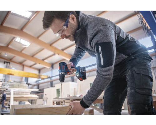Un homme portant des lunettes de protection utilise une visseuse sans fil pour travailler une pièce de bois.