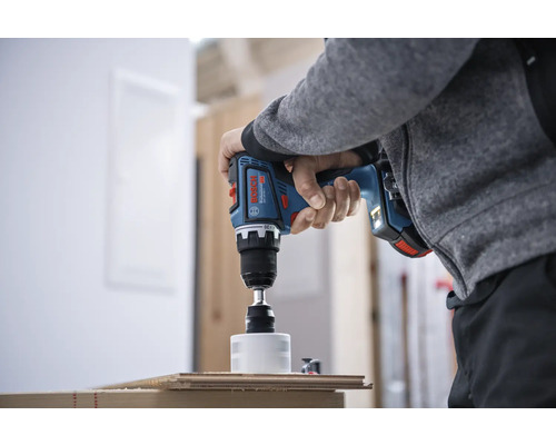 Une personne perce un trou dans une planche en bois avec une perceuse-visseuse sans fil.