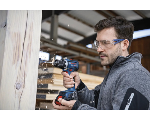 Un homme perce un morceau de bois avec une perceuse-visseuse sans fil