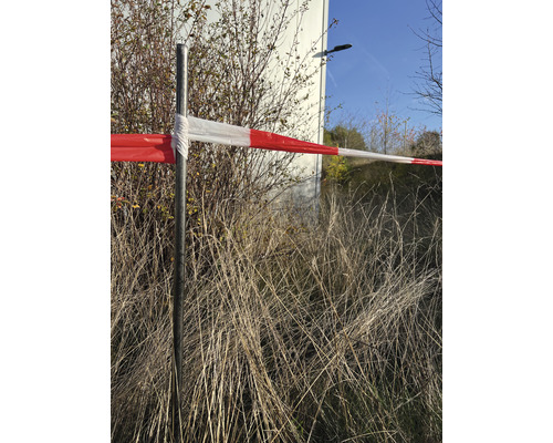 Ruban de sécurité sur un poteau métallique devant des buissons et de l''herbe