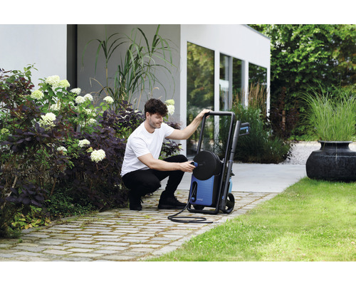 Un homme branche un nettoyeur haute pression dans un jardin.
