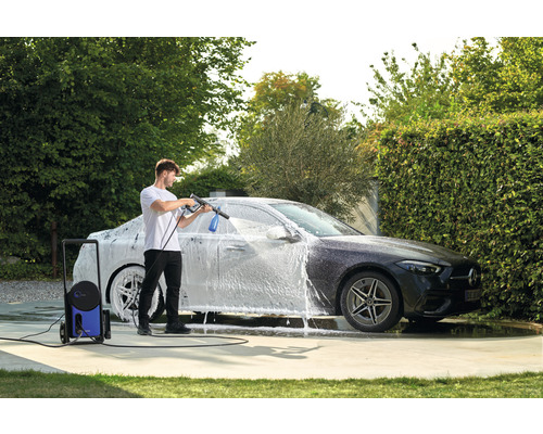 Un homme nettoie une voiture avec un nettoyeur haute pression dans le jardin.