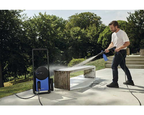 Un homme nettoie un banc de jardin à l''extérieur avec un nettoyeur haute pression.