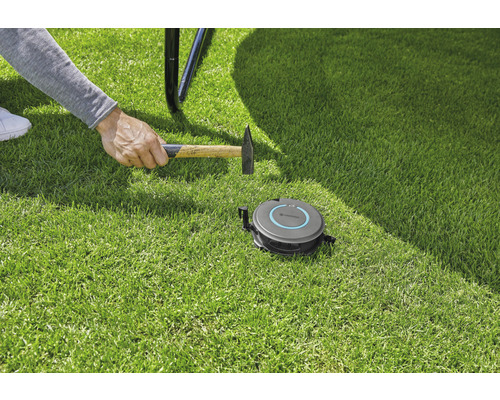 Installation d''un robot tondeuse Gardena avec un marteau sur une pelouse.