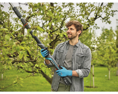 Un homme utilise un ébrancheur à batterie Gardena pour tailler des branches dans le jardin.