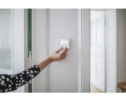 Eine Person bedient ein Bosch Smart Home Thermostat an einer Wand.